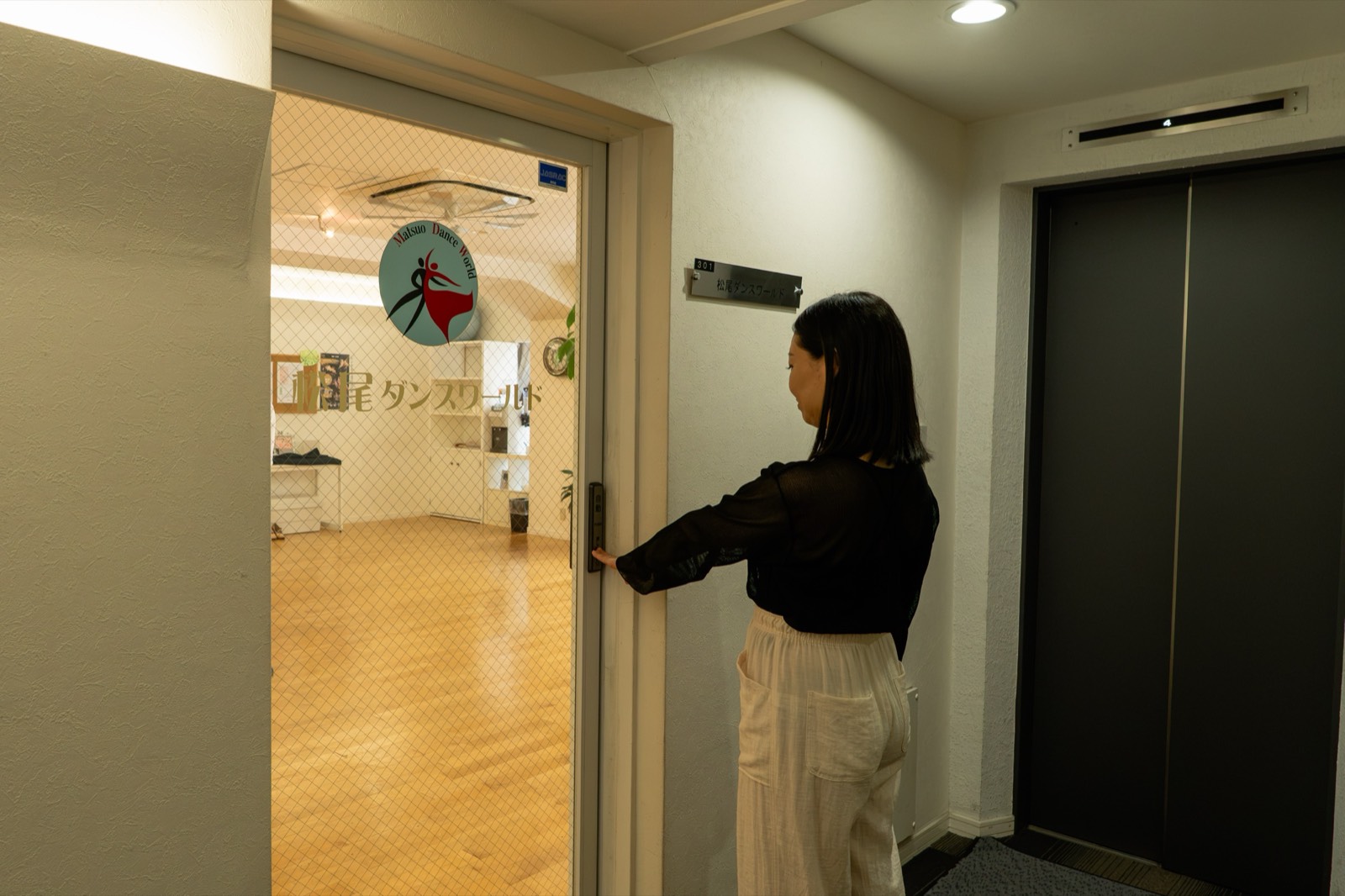3階のエレベーターホールで、スタジオの入口の扉を開ける女性